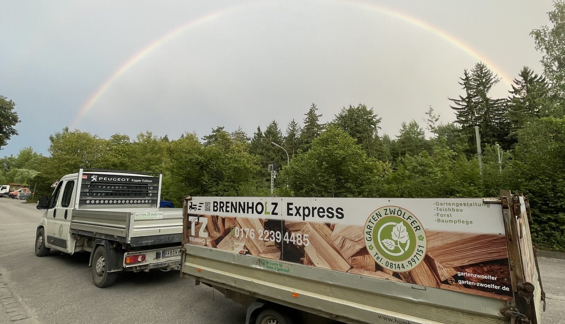 Brennholzexpress mit wolkigem Himmel und Regenbogen im Himmel